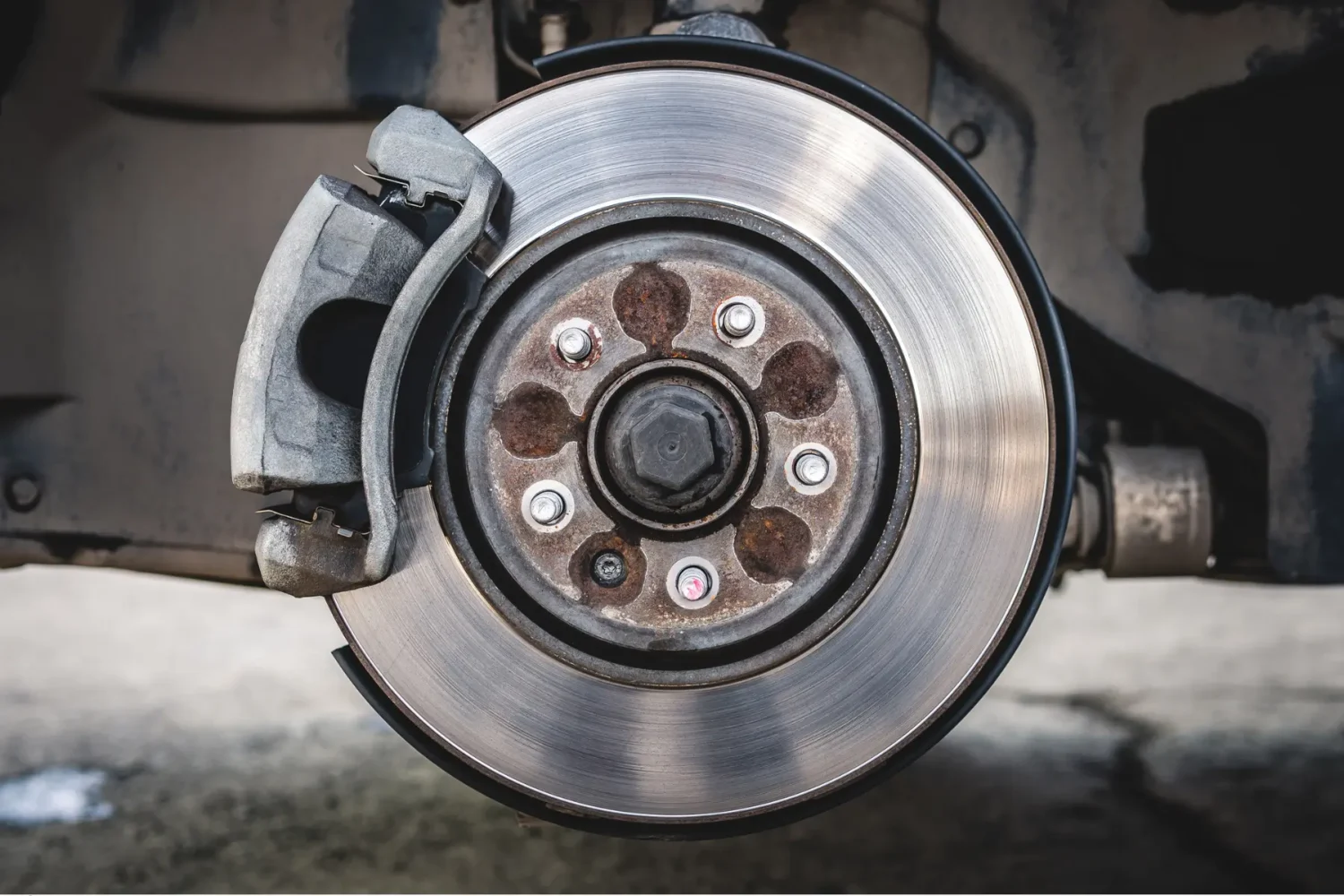 Exposed car brake rotor with visible rust on the hub and a gray caliper