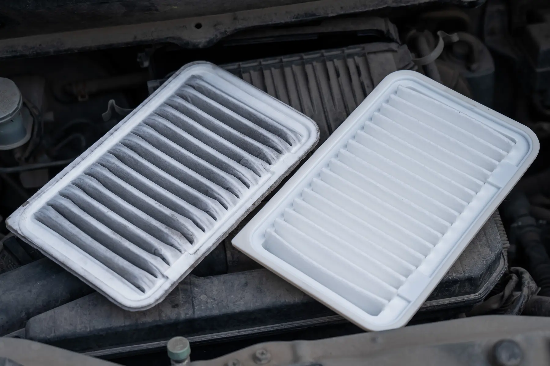 Comparison of a dirty and clean paper car air filter placed on an engine for inspection