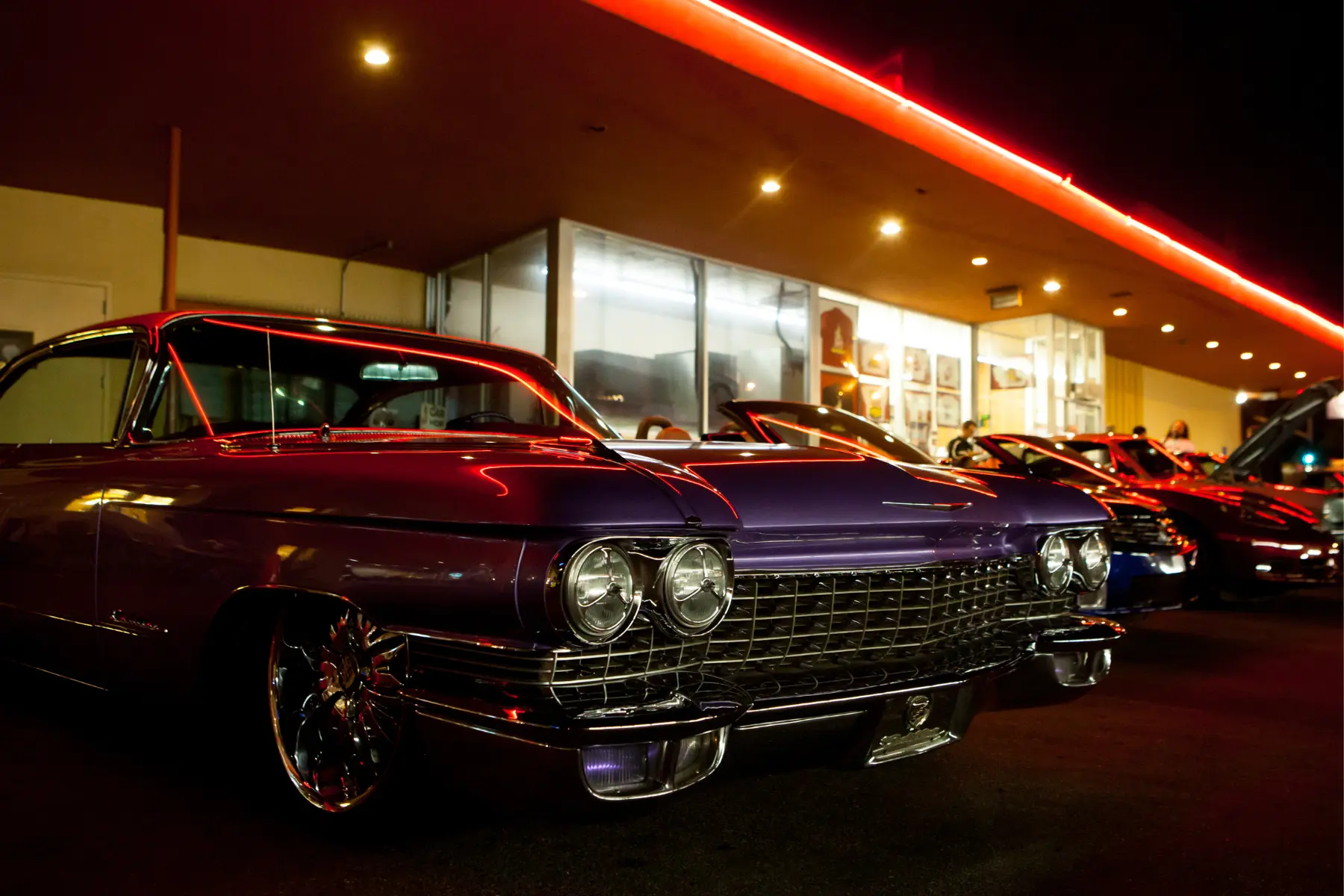 Vintage purple classic car with chrome detailing under neon lights at a retro-style car meet